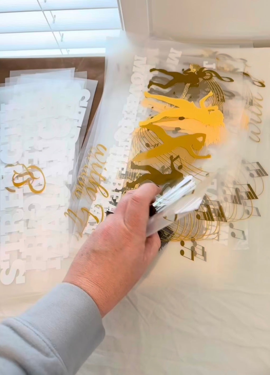 Hand using a tool to apply gold leaf design to a surface with decorative elements.